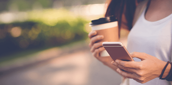 Female outside looking at phone holding coffee