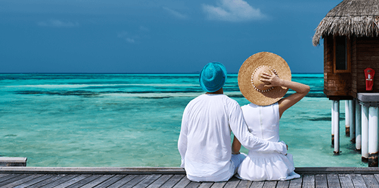two people sitting on a dock looking out at the ocean at a tropical destination