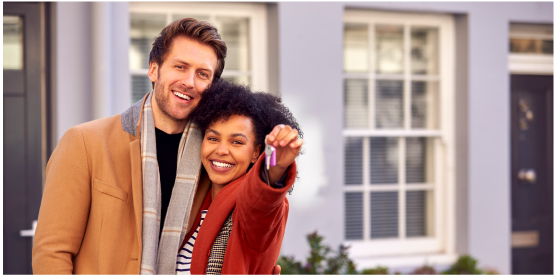 smiling couple holding keys outside their new home