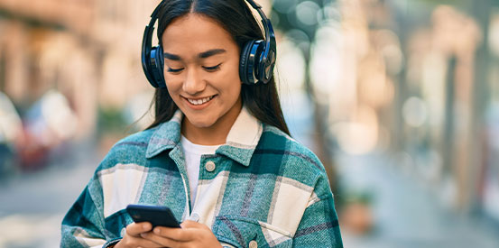 Young latin girl smiling happy using smartphone and headphones at the city.